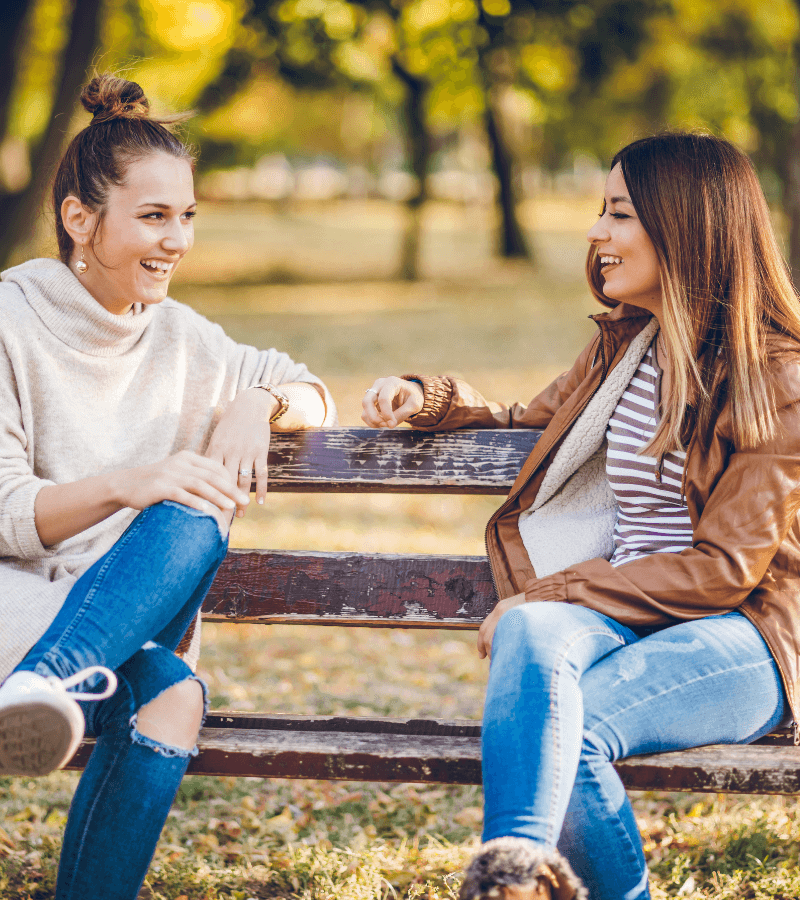 women smiling and talking on a park bench